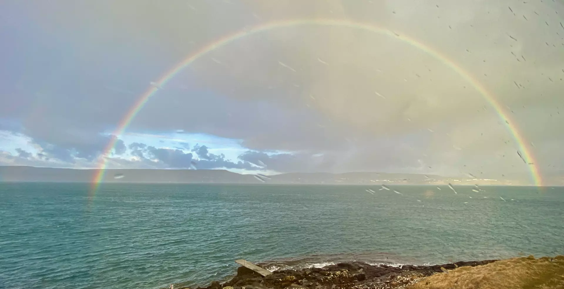 Fyrstu 2-3 vikurnar í apríl høvdu vit lágtrýstveður. Hann lá nógv millum landsynning og útsynning. Tað vóru løtur við hugaligum skýlofti og hampuligum veðri, men ofta var grátt og vátt. Um morgunin 13. apríl otaði eitt samanrunnið brúgvalag seg inn yvir landið av landsynningi. Tað regnaði, og ælabogar sóust vakrir á luftini, sum her á myndini – tikin um morgunin úr Nólsoy inn á Tangafjørð. Mynd: Rógvi Rasmussen.