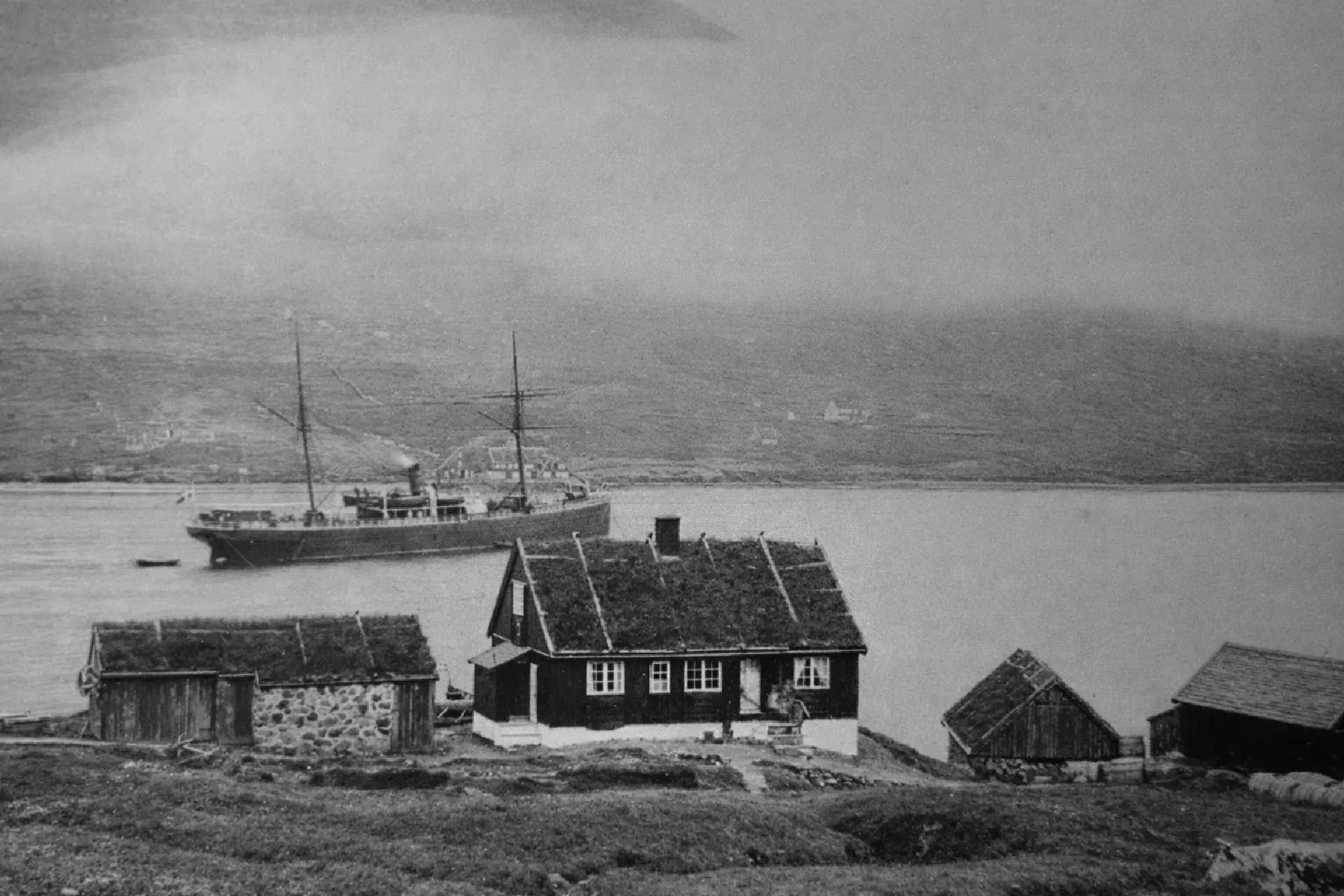 Myndin er frá 1892 og húsini á myndini eru sethúsini hjá Nickels Lutzen. Skipið á Vánni er ‘Laura’, sum silgdi fyri ‘Det Forenede Dampskip Selskab’ í Norðuratlantshavinum frá 1888 til 1910.